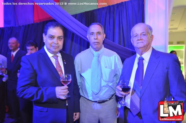 three men stand together while drinking wine