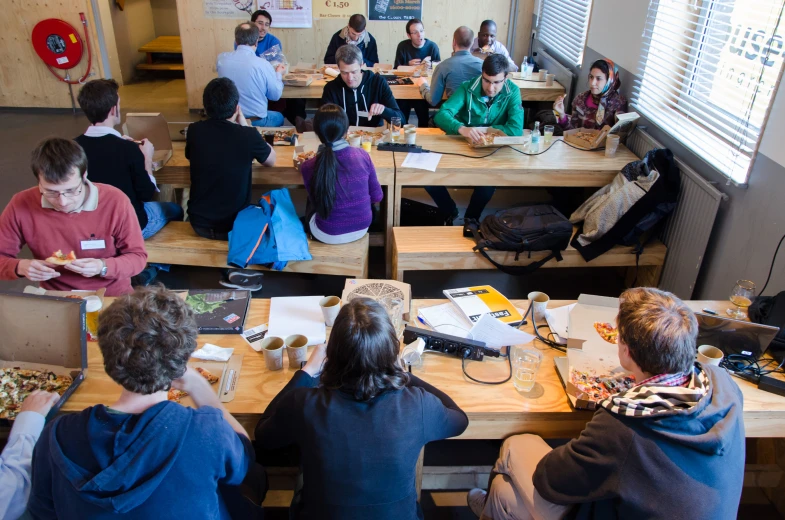 group of people sitting at long wooden tables with laptops on them