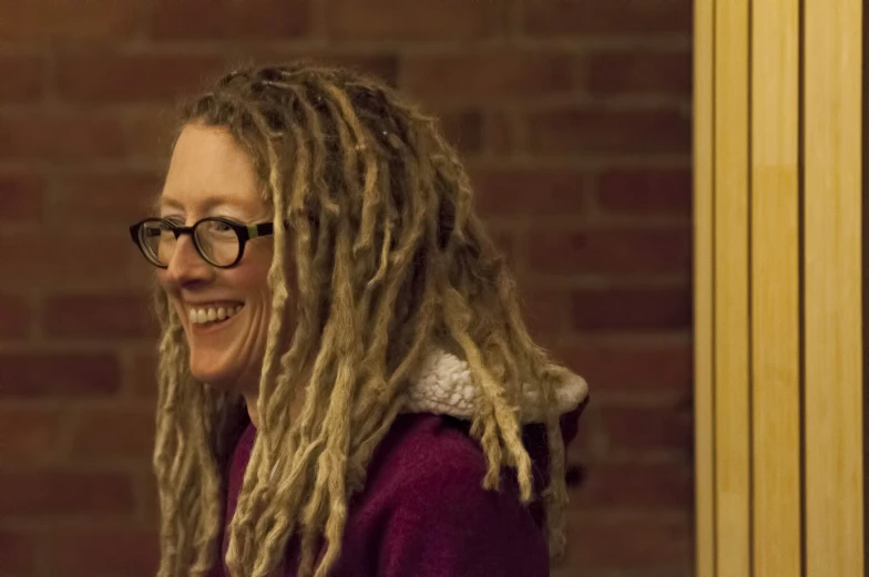 a woman with long dreadlocks is wearing a purple sweater and is smiling