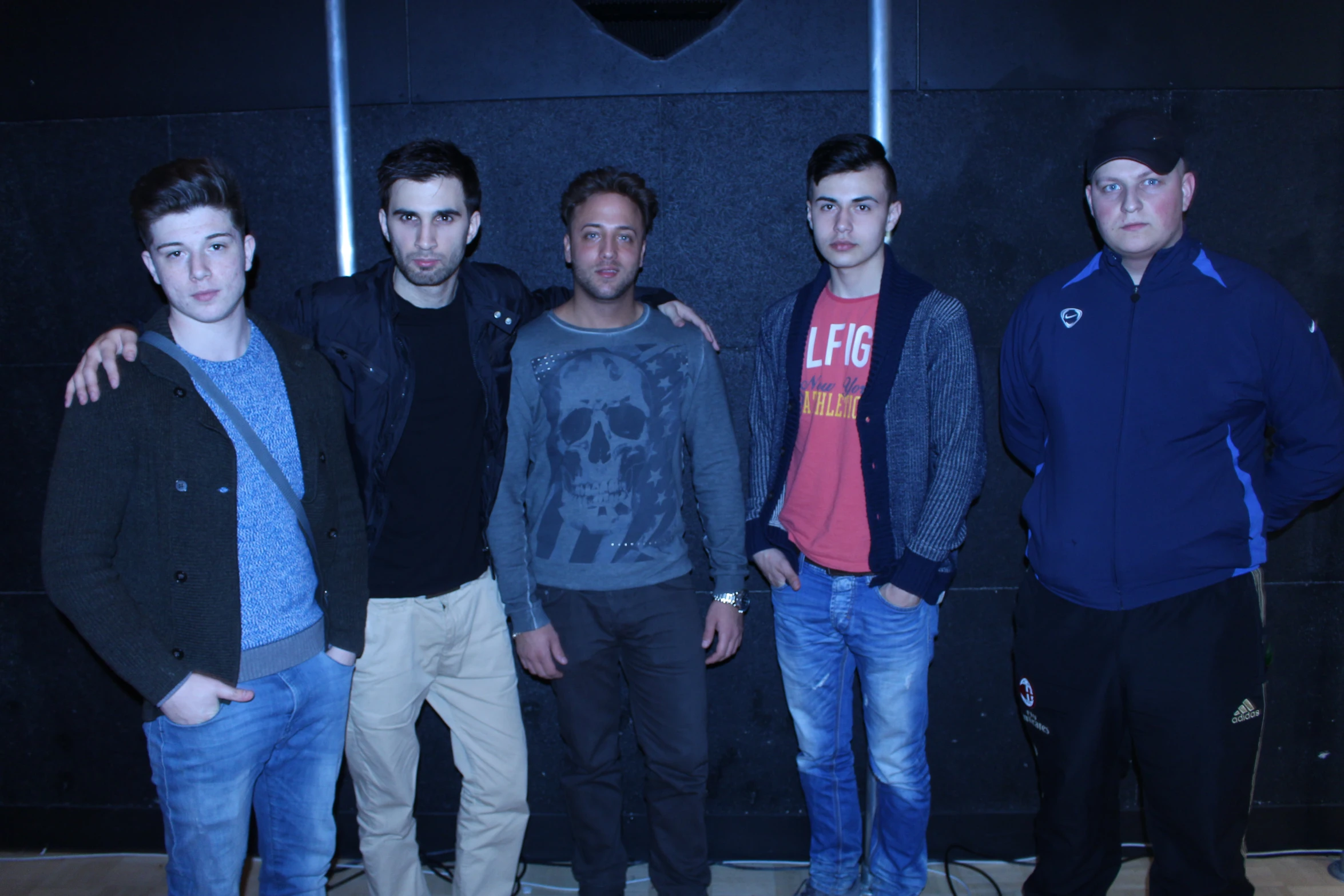 four males posing for a picture and a black wall in the background