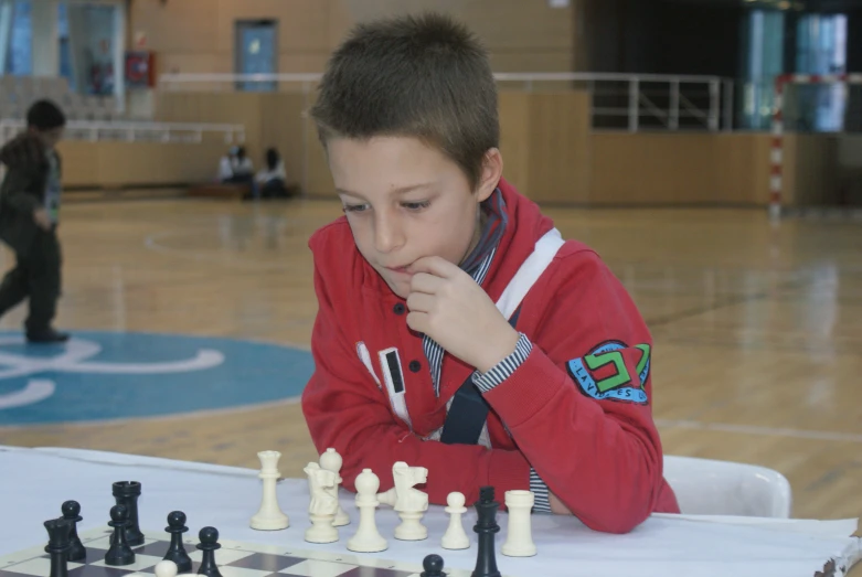 boy playing chess in a gym with other people