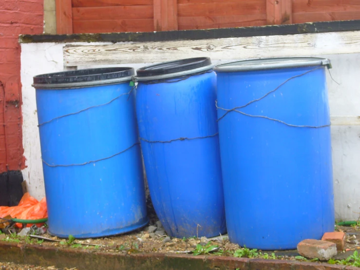 three blue drums with two trash bags under them in front of a brick wall