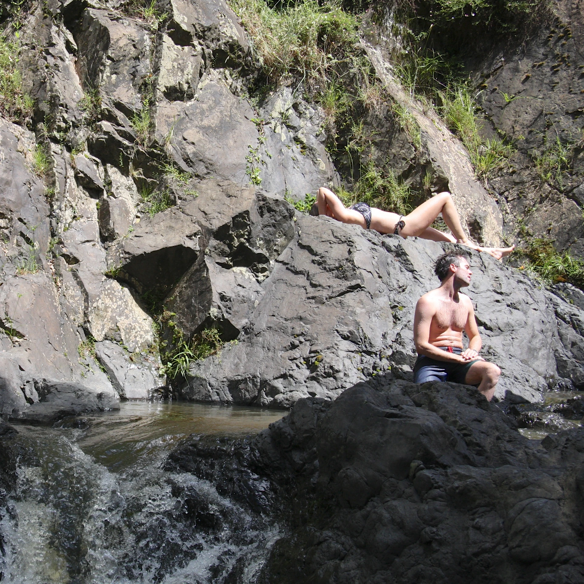 the couple is sitting on a rock next to the river