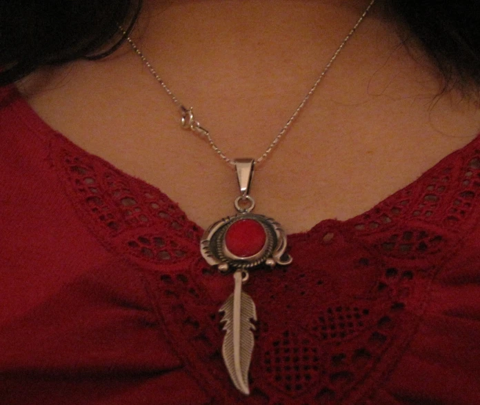 this red shirt is adorned with an antique style pendant and a feather