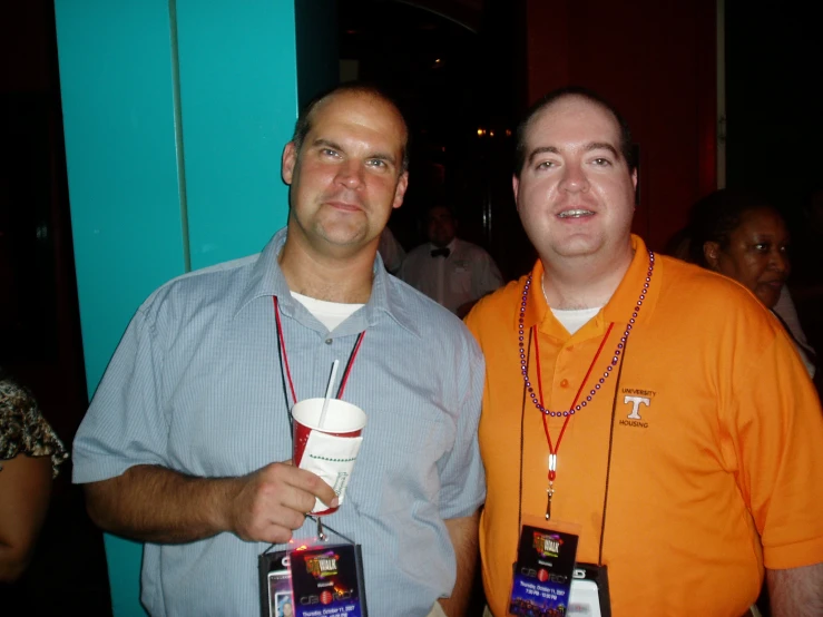 a man holding a white cup while standing next to a man in an orange shirt