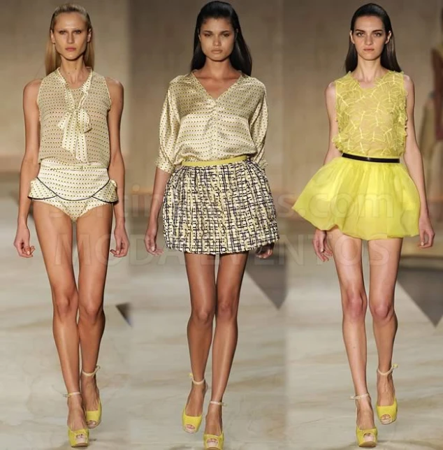 four women walking down a runway in short yellow skirts