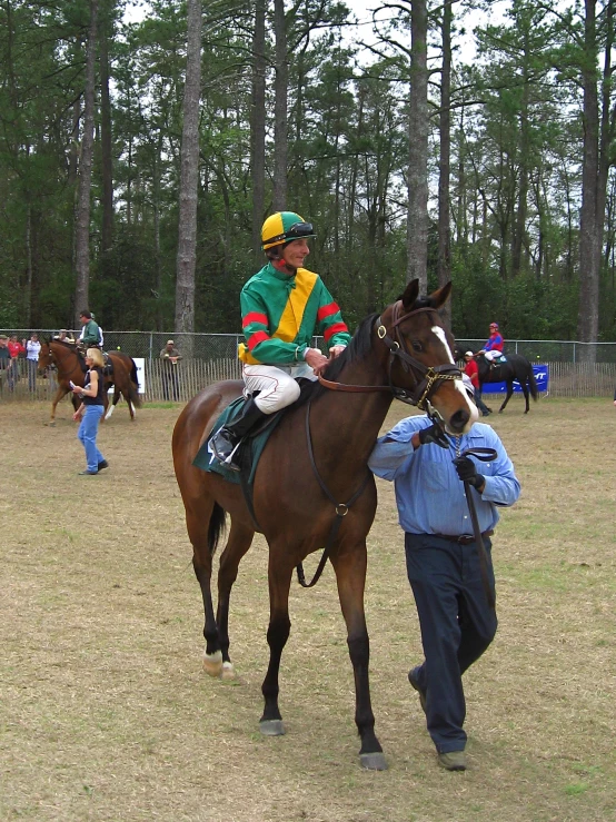 jockey on horseback leading on in grassy field