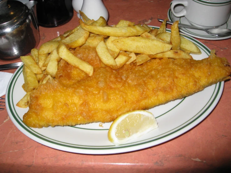 a fish and chips plate on a table with two silver mugs