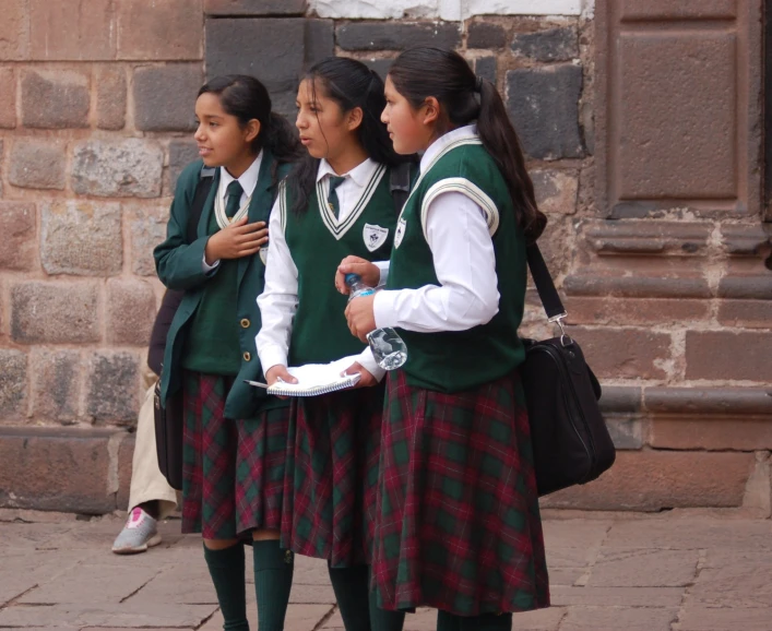 three girls in school uniforms stand near a building