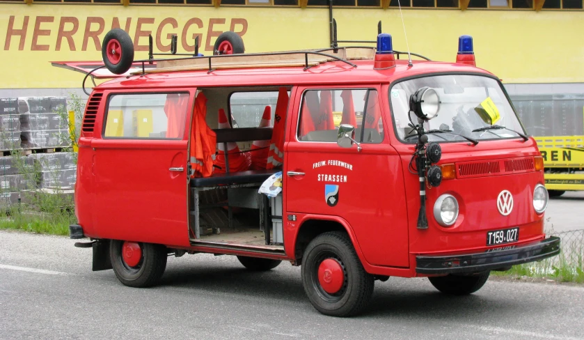 an old, red van parked on the street in front of a large yellow building
