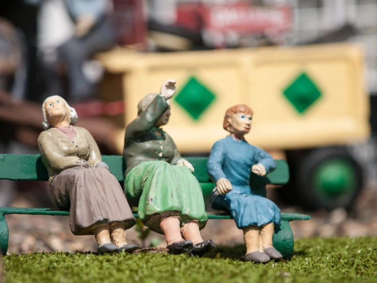 three miniature people sitting on a bench looking at a garbage truck