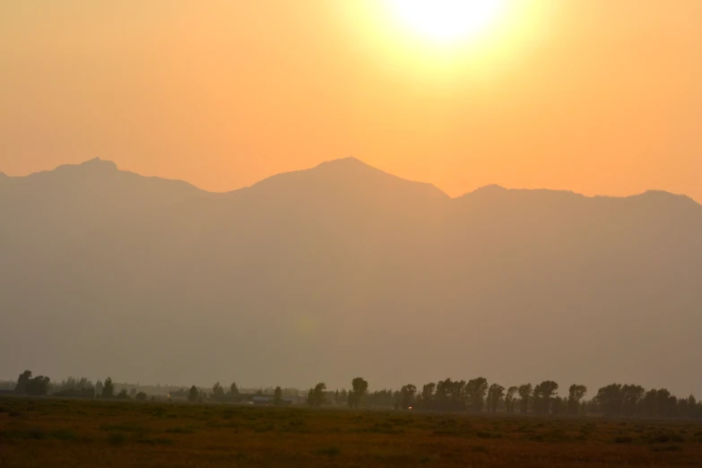 the sun is setting over a mountain range in a field