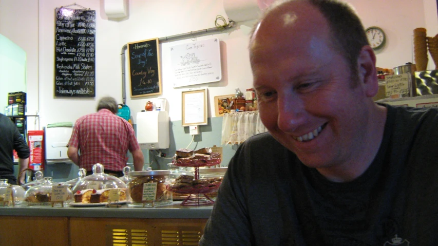 a man smiles at the camera behind a counter in a cafe