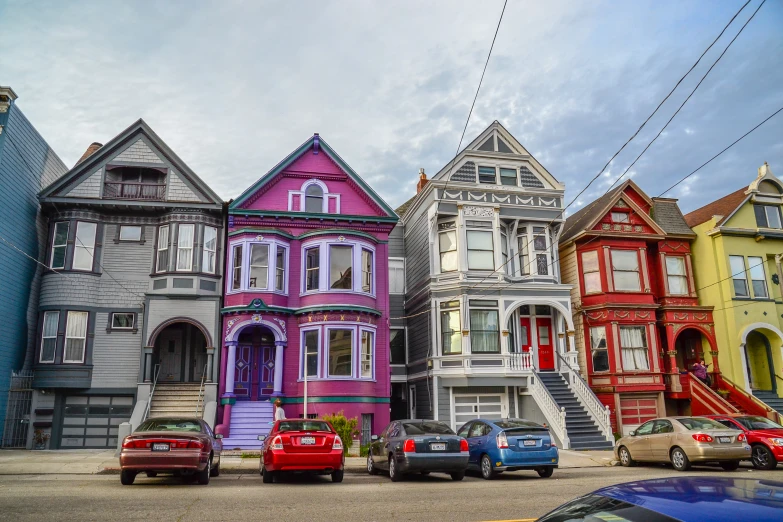 various colored victorian homes on a hill next to cars