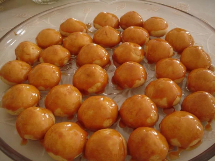 a glass platter full of donuts covered in a brown sauce