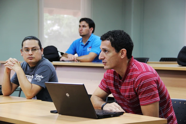 three students in a classroom sitting at desks working on computers