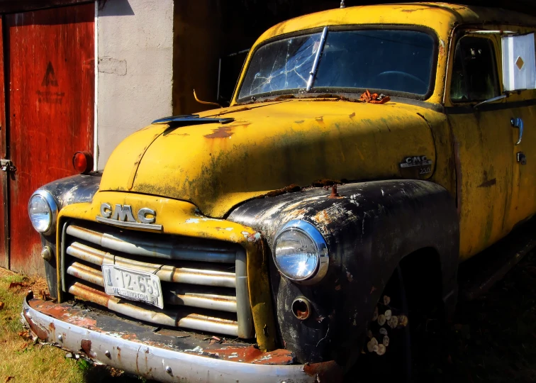 an old yellow truck sitting outside of a barn