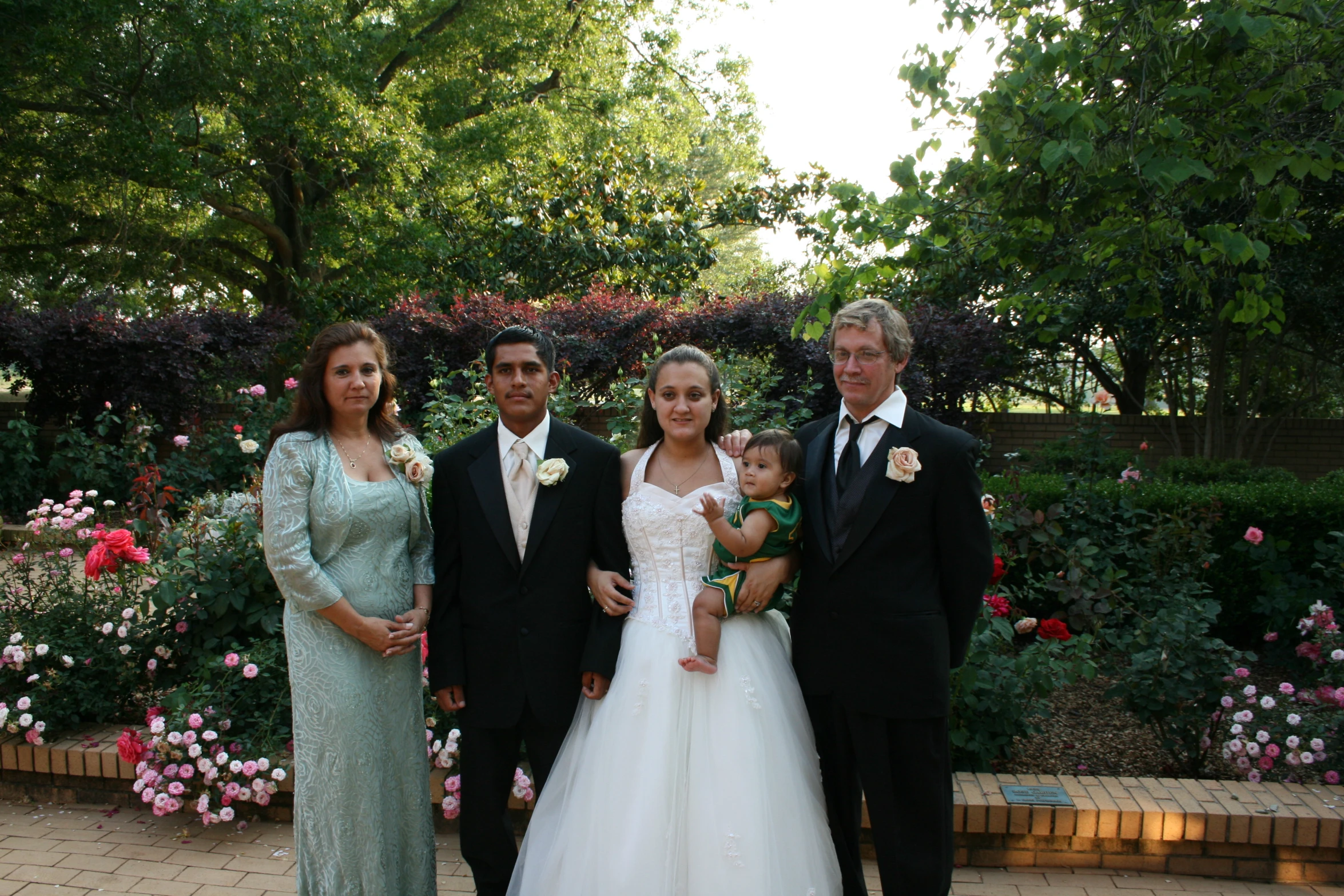 a man in a suit and a woman in a gown hold a baby while two other people pose for the camera