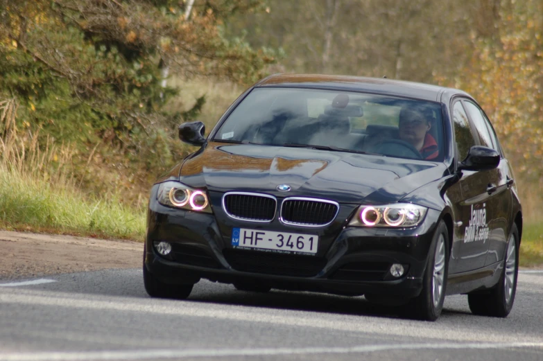 the front of a black bmw car driving on a road