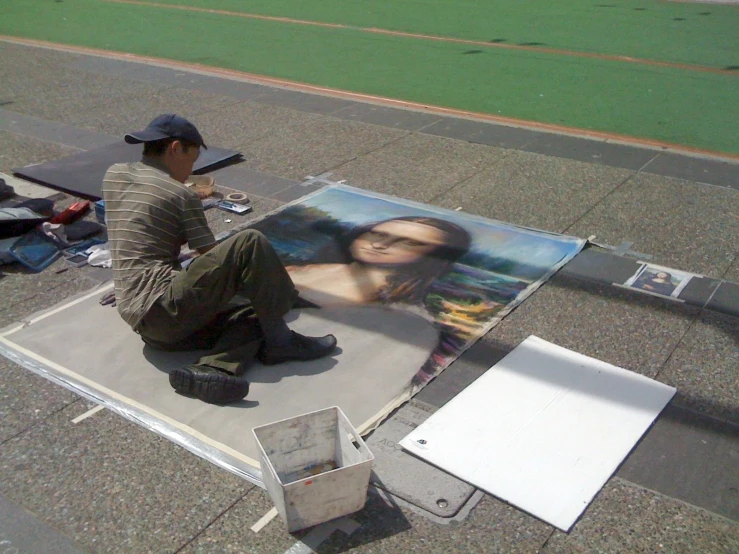 a man sitting on the pavement painting with a portrait of a woman