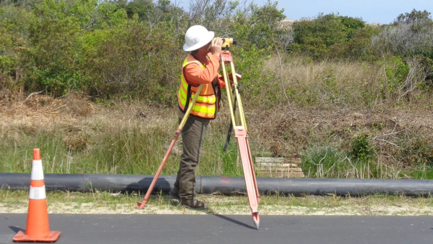 a man holding a pole, standing on the road next to orange cones