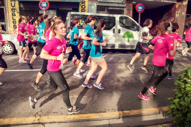runners in pink shirts run past a van on the street
