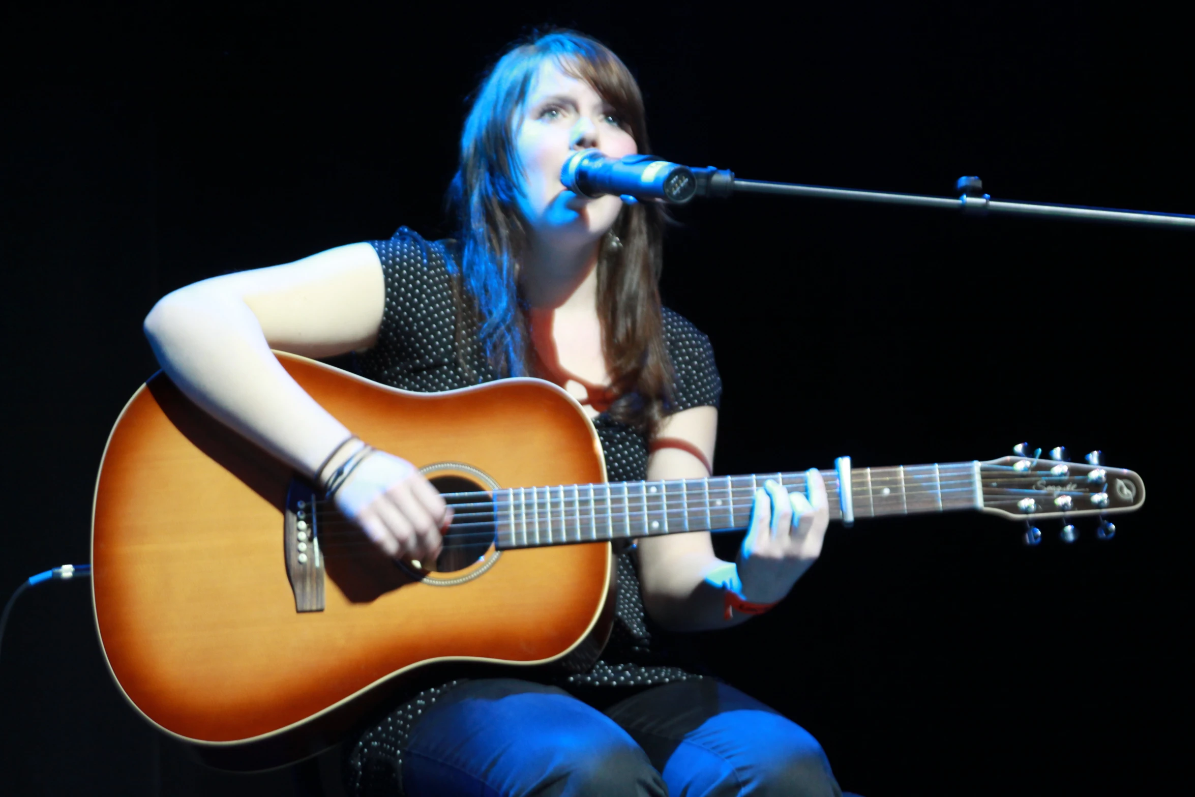 the girl is playing her guitar while singing into a microphone