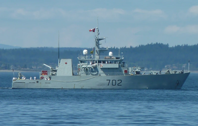 large naval ship in the water with a canadian flag flying on top