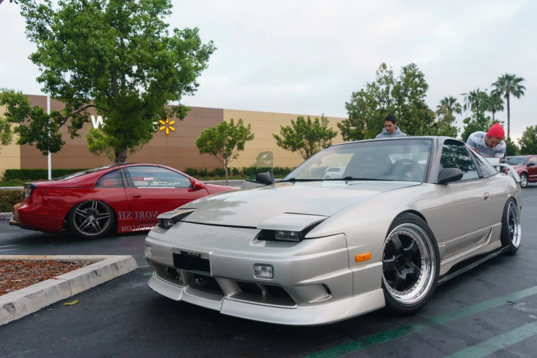 two people in a silver and black sports car and a red car