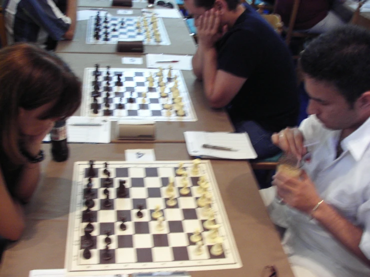 three people sitting at a table with chess boards on the table