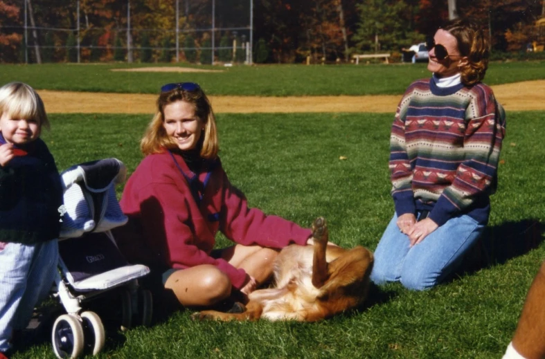 two women, one child, and a dog are sitting on the grass