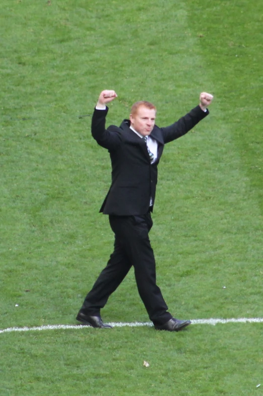 a man in a black suit and tie walks on a field