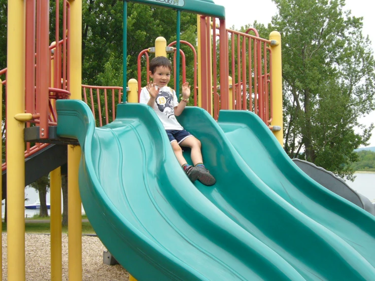 a little boy sits at the top of a slide