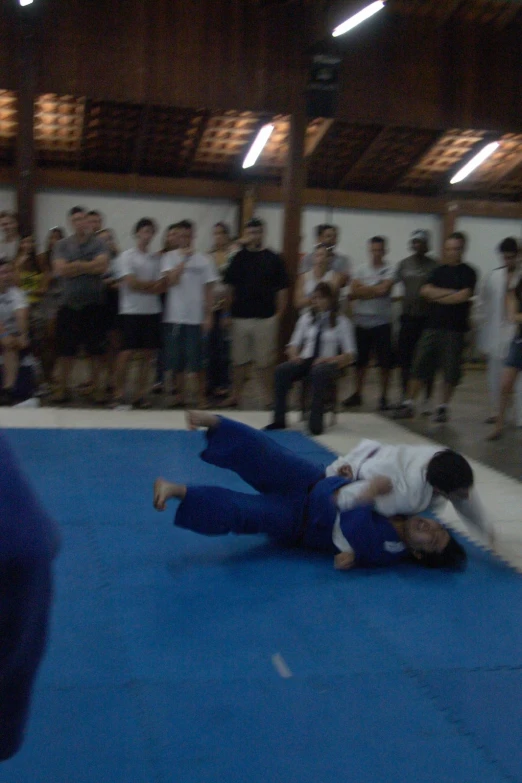 a group of people watching a man performing a flip on a wrestling mat