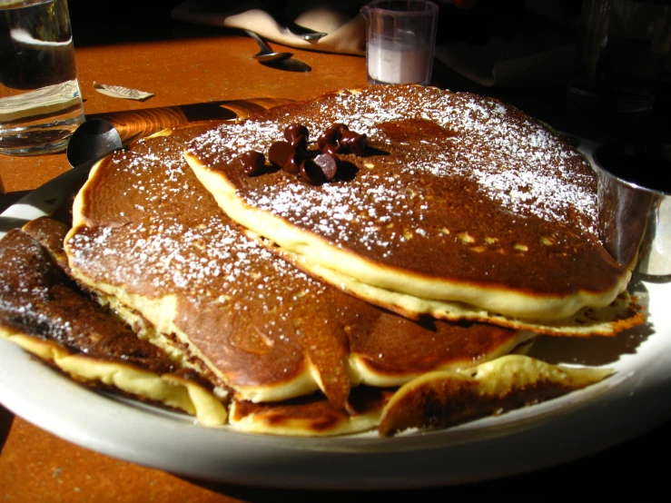 three large pancakes on a plate with syrup and walnuts