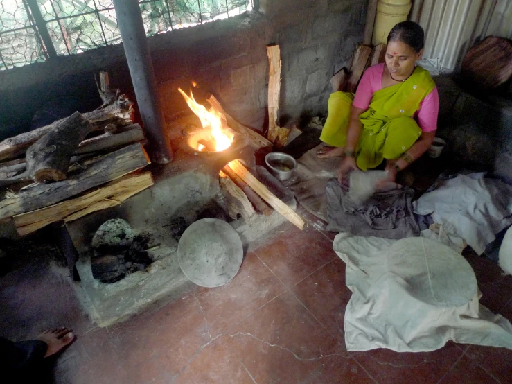 a woman sitting by the fire and cooking in a hut