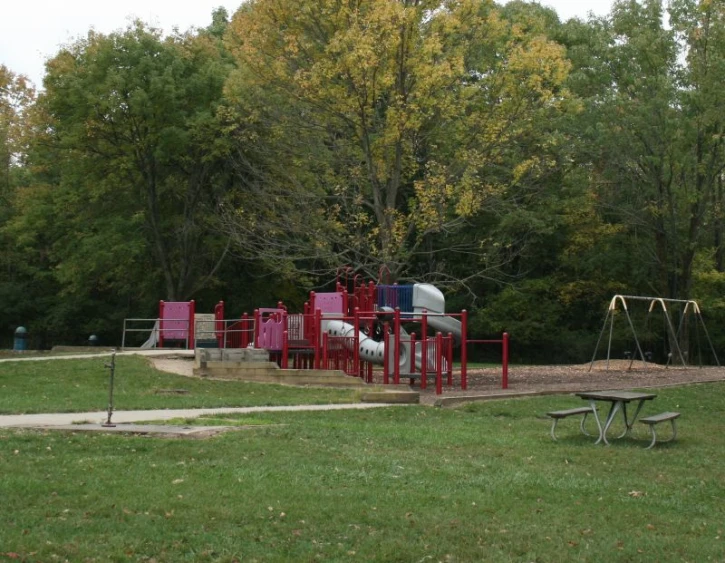 an empty playground with swings, a slide and a small bench
