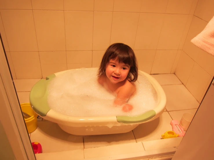 a child smiles while standing in a bath tub