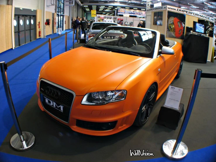 an orange convertible sports car sitting in front of a blue and black carpet