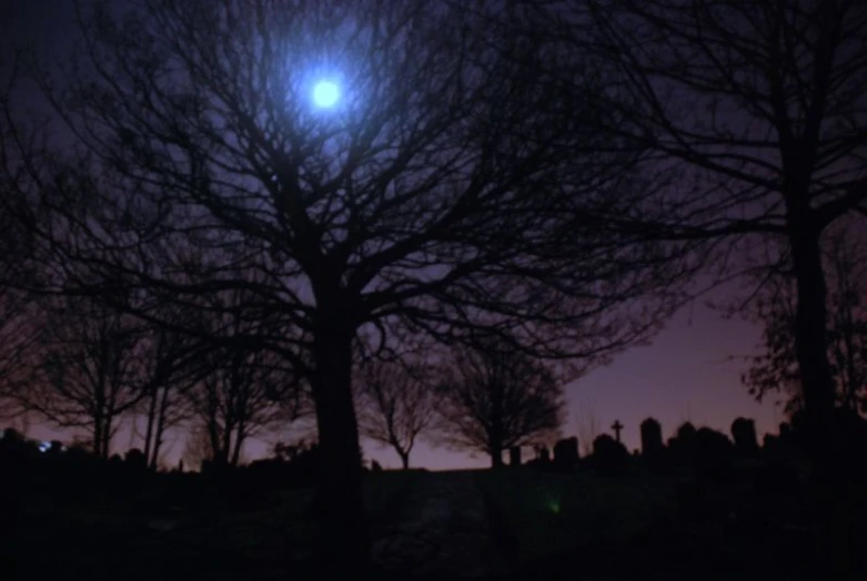 the full moon is setting over a cemetery in a dark night