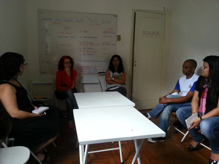 four people sitting on a chair in an office with a white board behind them