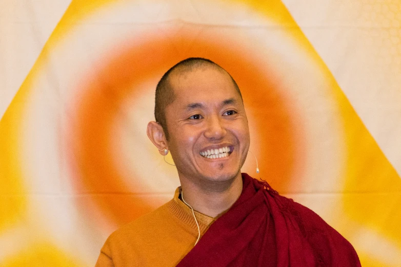 a young monk wearing orange and gold robes with yellow circular background