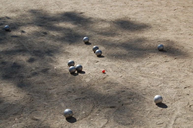 several balls laying on a dirt ground in front of a tree