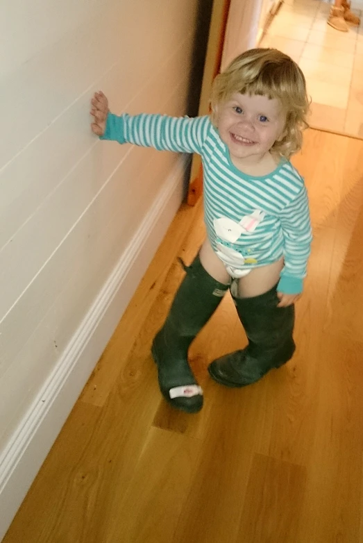 a toddler girl in her well - loved outfit standing by the wall