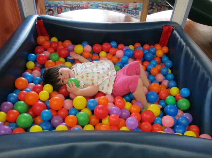 a little girl that is laying in some balls