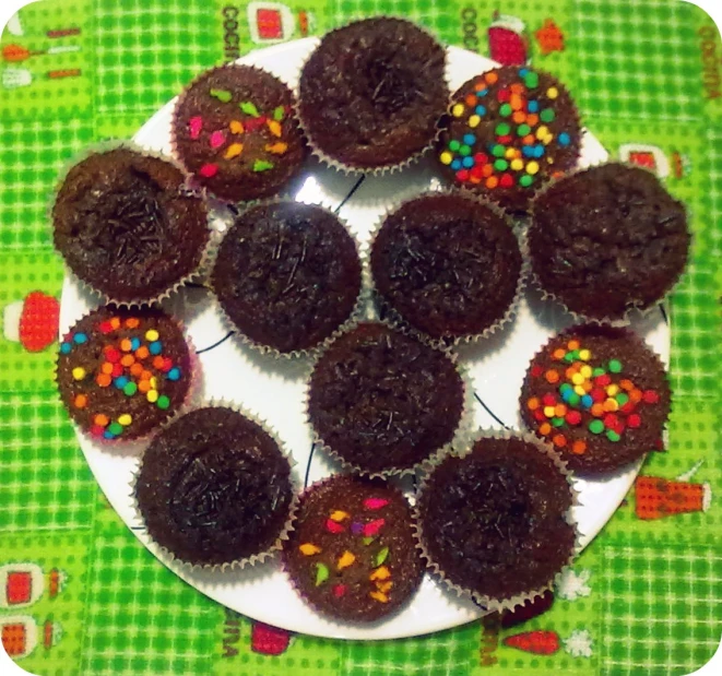 a white plate holding several chocolate cupcakes with sprinkles