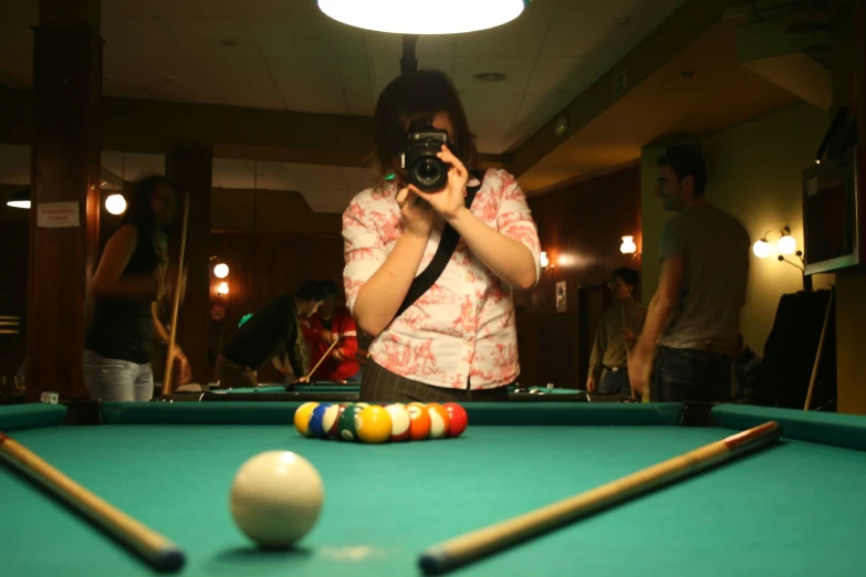 people are playing pool and a woman is taking a picture