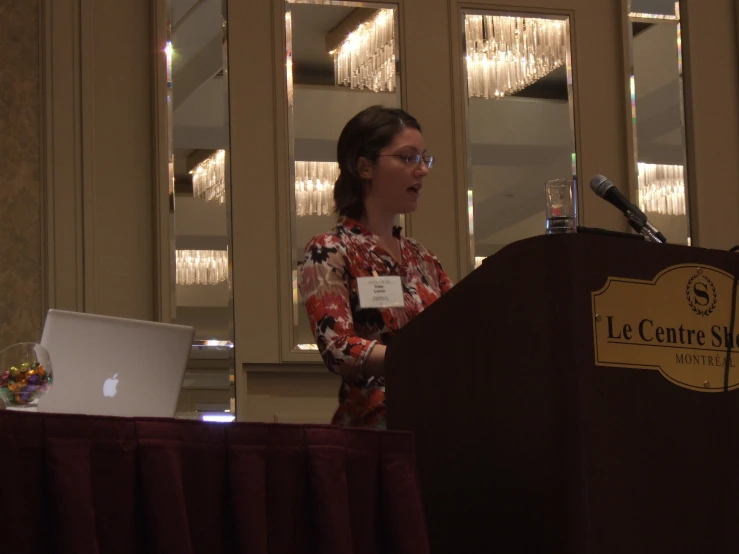 a woman speaking from the podium next to a laptop