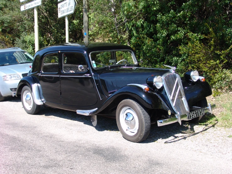 an old model car in the road next to some trees