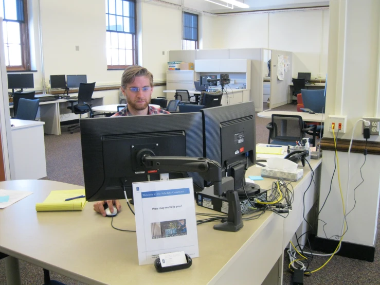 man with multiple monitors in office setting near table